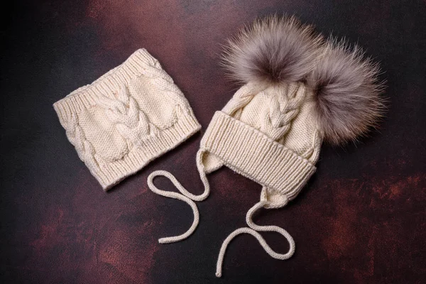 Beautiful white knitted winter cap with pompons on a dark concrete background. Clothes for winter cold