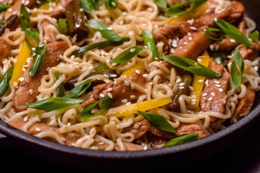 Lezzetli Asya yemekleri pilav eriştesi, tavuk, kuşkonmaz, biber, susam tohumu ve soya sosu ile koyu beton arka planda.