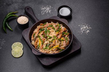 Lezzetli Asya yemekleri pilav eriştesi, tavuk, kuşkonmaz, biber, susam tohumu ve soya sosu ile koyu beton arka planda.