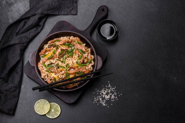 Lezzetli Asya yemekleri pilav eriştesi, tavuk, kuşkonmaz, biber, susam tohumu ve soya sosu ile koyu beton arka planda.