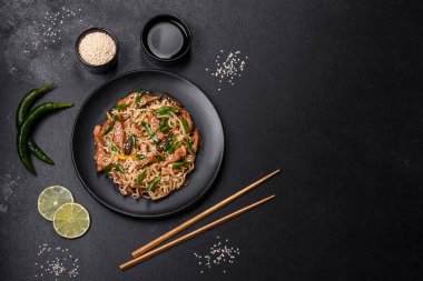 Lezzetli Asya yemekleri pilav eriştesi, tavuk, kuşkonmaz, biber, susam tohumu ve soya sosu ile koyu beton arka planda.
