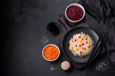 Lezzetli Asya yemeği, pirinç, biber, baharat ve otlar siyah bir tabakta koyu beton arka planda.