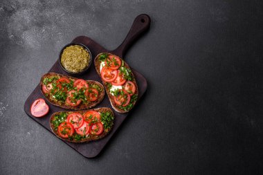 Domatesli lezzetli bruschetta, mozzarella, fesleğen, baharat ve otlar koyu beton arka planda.