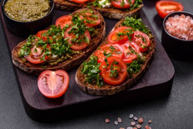 Domatesli lezzetli bruschetta, mozzarella, fesleğen, baharat ve otlar koyu beton arka planda.