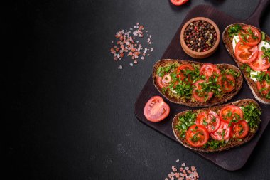 Domatesli lezzetli bruschetta, mozzarella, fesleğen, baharat ve otlar koyu beton arka planda.