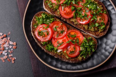 Domatesli lezzetli bruschetta, mozzarella, fesleğen, baharat ve otlar koyu beton arka planda.