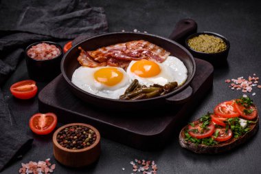 Lezzetli kahvaltı yumurta, domuz pastırması, fasulye, domates, esmer çimento arka planda baharatlar ve otlardan oluşur.