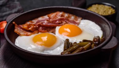 Lezzetli kahvaltı yumurta, domuz pastırması, fasulye, domates, esmer çimento arka planda baharatlar ve otlardan oluşur.