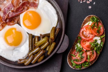 Lezzetli kahvaltı yumurta, domuz pastırması, fasulye, domates, esmer çimento arka planda baharatlar ve otlardan oluşur.