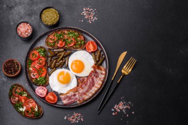 Lezzetli kahvaltı yumurta, domuz pastırması, fasulye, domates, esmer çimento arka planda baharatlar ve otlardan oluşur.