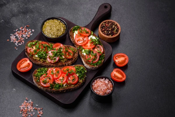 stock image Tasty bruschetta with tomatoes, mozzarella, basil, spices and herbs on a dark concrete background