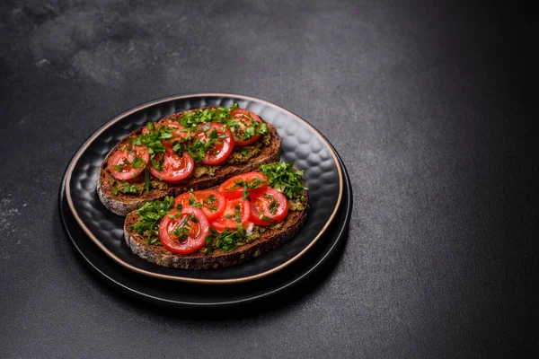 stock image Tasty bruschetta with tomatoes, mozzarella, basil, spices and herbs on a dark concrete background