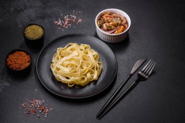 Pesto soslu lezzetli taze makarna ve siyah bir tabakta koyu beton arka planda deniz ürünleri.