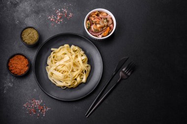 Pesto soslu lezzetli taze makarna ve siyah bir tabakta koyu beton arka planda deniz ürünleri.