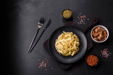Pesto soslu lezzetli taze makarna ve siyah bir tabakta koyu beton arka planda deniz ürünleri.