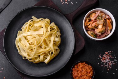 Pesto soslu lezzetli taze makarna ve siyah bir tabakta koyu beton arka planda deniz ürünleri.