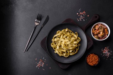 Pesto soslu lezzetli taze makarna ve siyah bir tabakta koyu beton arka planda deniz ürünleri.