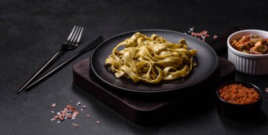 Pesto soslu lezzetli taze makarna ve siyah bir tabakta koyu beton arka planda deniz ürünleri.