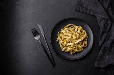 Pesto soslu lezzetli taze makarna ve siyah bir tabakta koyu beton arka planda deniz ürünleri.