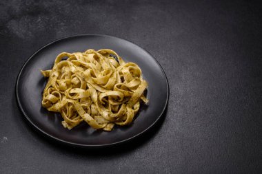 Pesto soslu lezzetli taze makarna ve siyah bir tabakta koyu beton arka planda deniz ürünleri.