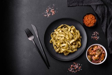Pesto soslu lezzetli taze makarna ve siyah bir tabakta koyu beton arka planda deniz ürünleri.