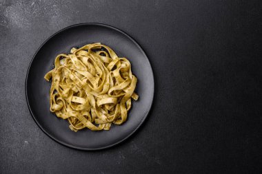 Pesto soslu lezzetli taze makarna ve siyah bir tabakta koyu beton arka planda deniz ürünleri.