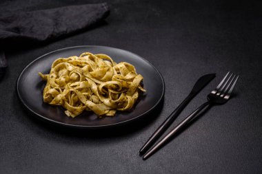 Pesto soslu lezzetli taze makarna ve siyah bir tabakta koyu beton arka planda deniz ürünleri.