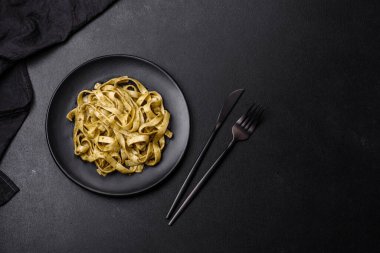 Pesto soslu lezzetli taze makarna ve siyah bir tabakta koyu beton arka planda deniz ürünleri.