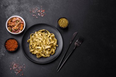Pesto soslu lezzetli taze makarna ve siyah bir tabakta koyu beton arka planda deniz ürünleri.