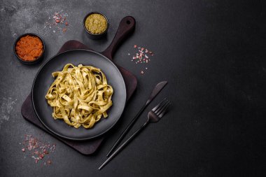 Pesto soslu lezzetli taze makarna ve siyah bir tabakta koyu beton arka planda deniz ürünleri.