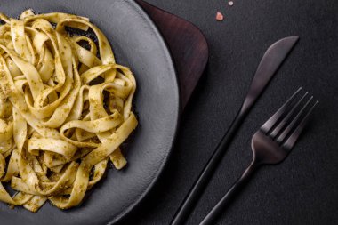 Pesto soslu lezzetli taze makarna ve siyah bir tabakta koyu beton arka planda deniz ürünleri.