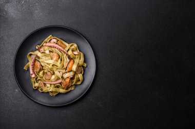 Pesto soslu lezzetli taze makarna ve siyah bir tabakta koyu beton arka planda deniz ürünleri.