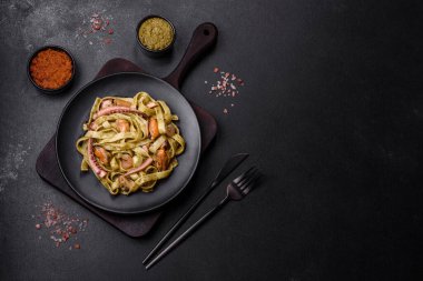 Pesto soslu lezzetli taze makarna ve siyah bir tabakta koyu beton arka planda deniz ürünleri.