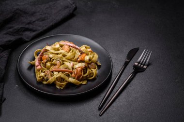 Pesto soslu lezzetli taze makarna ve siyah bir tabakta koyu beton arka planda deniz ürünleri.