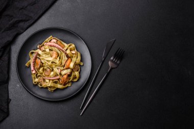 Pesto soslu lezzetli taze makarna ve siyah bir tabakta koyu beton arka planda deniz ürünleri.