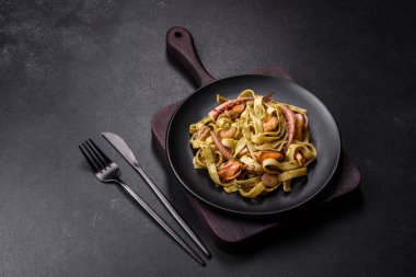 Pesto soslu lezzetli taze makarna ve siyah bir tabakta koyu beton arka planda deniz ürünleri.