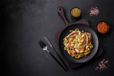 Pesto soslu lezzetli taze makarna ve siyah bir tabakta koyu beton arka planda deniz ürünleri.