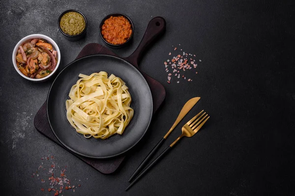 Pesto soslu lezzetli taze makarna ve siyah bir tabakta koyu beton arka planda deniz ürünleri.