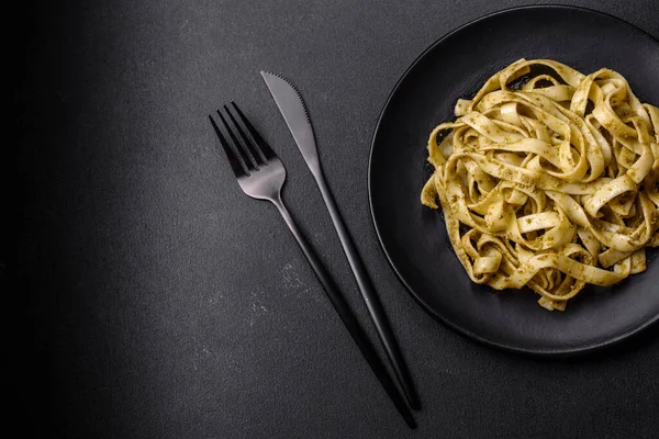 Pesto soslu lezzetli taze makarna ve siyah bir tabakta koyu beton arka planda deniz ürünleri.