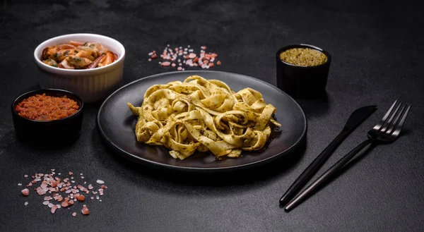 Pesto soslu lezzetli taze makarna ve siyah bir tabakta koyu beton arka planda deniz ürünleri.