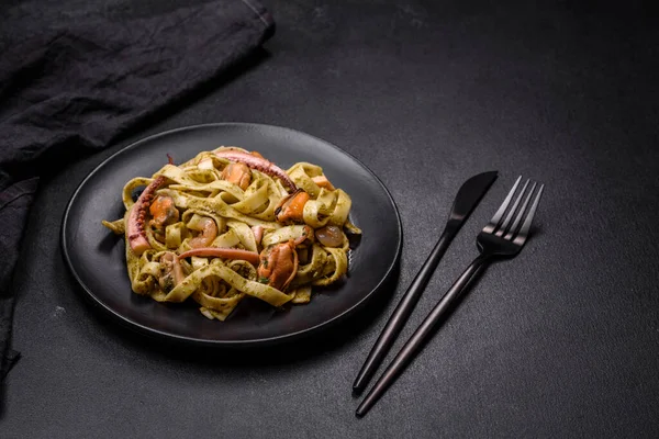 Pesto soslu lezzetli taze makarna ve siyah bir tabakta koyu beton arka planda deniz ürünleri.