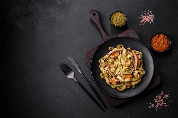 Pesto soslu lezzetli taze makarna ve siyah bir tabakta koyu beton arka planda deniz ürünleri.