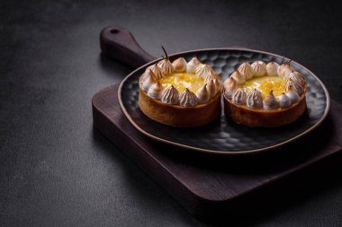 Limon aromalı lezzetli meyveli tart ve koyu beton arka planda siyah bir tabakta krema.