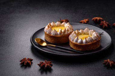 Limon aromalı lezzetli meyveli tart ve koyu beton arka planda siyah bir tabakta krema.