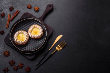 Limon aromalı lezzetli meyveli tart ve koyu beton arka planda siyah bir tabakta krema.