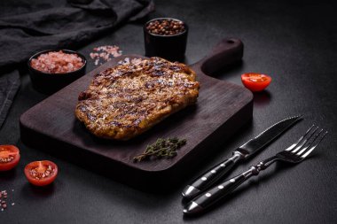 Lezzetli ızgara domuz bifteği, baharatlar ve otlar ahşap bir kesim tahtasının üzerinde.