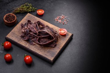 Lezzetli tuzlu kurutulmuş sığır eti. Koyu beton arka planda bira için aperatif olarak dilimlenmiş.