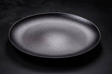 Koyu beton arka planda boş siyah seramik plaka. Aile yemeği için masayı hazırlıyorum.