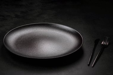 Koyu beton arka planda boş siyah seramik plaka. Aile yemeği için masayı hazırlıyorum.