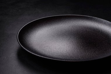 Koyu beton arka planda boş siyah seramik plaka. Aile yemeği için masayı hazırlıyorum.